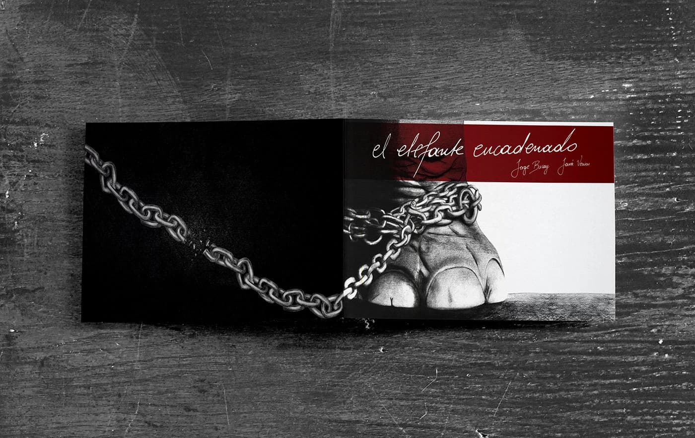 The Chained Elephant open on a dark wooden table, a chain running across the spread to the elephant’s foot